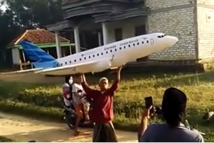 Tangkapan layar video yang memperlihatkan seorang pria mengenakan sarung dan peci, tengah menerbangkan miniatur pesawat Garuda Indonesia.