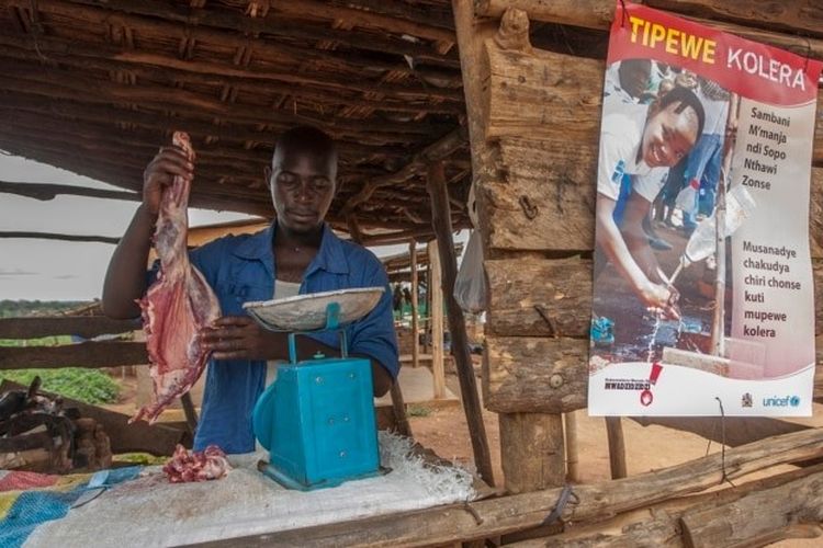 Seorang tukang daging menyiapkan daging kambing di samping poster UNICEF yang menyerukan orang-orang untuk mengambil tindakan pencegahan untuk melindungi diri dari kolera, di Likuni, di luar Lilongwe, Malawi, 27 Januari 2018. 