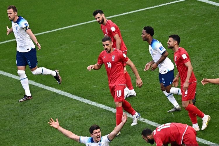 Bek Inggris Harry Maguire (tengah) bereaksi setelah ditahan oleh bek Iran Roozbeh Cheshmi pada laga Grup B Piala Dunia Qatar 2022 antara Inggris vs Iran di Stadion Internasional Khalifa di Doha pada Senin 21 November 2022.
