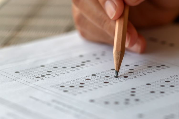 Student hand testing doing test exam with pencil drawing selected choices on answer sheet in school final exams at college or university. Taking multiple choice for assessment in examination classroom