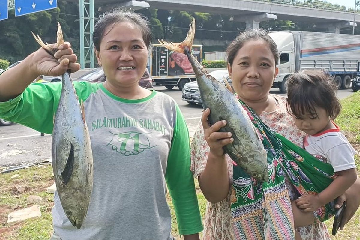 Dewi (kiri), satu dari beberapa emak-emak yang juga warga sekitar saat mendapat seekor tongkol gratis usai kecelakaan mobil pengangkut ikan beku di Tol Jatibening KM 8 mengarah ke Jakarta pada Rabu (12/4/2023).
