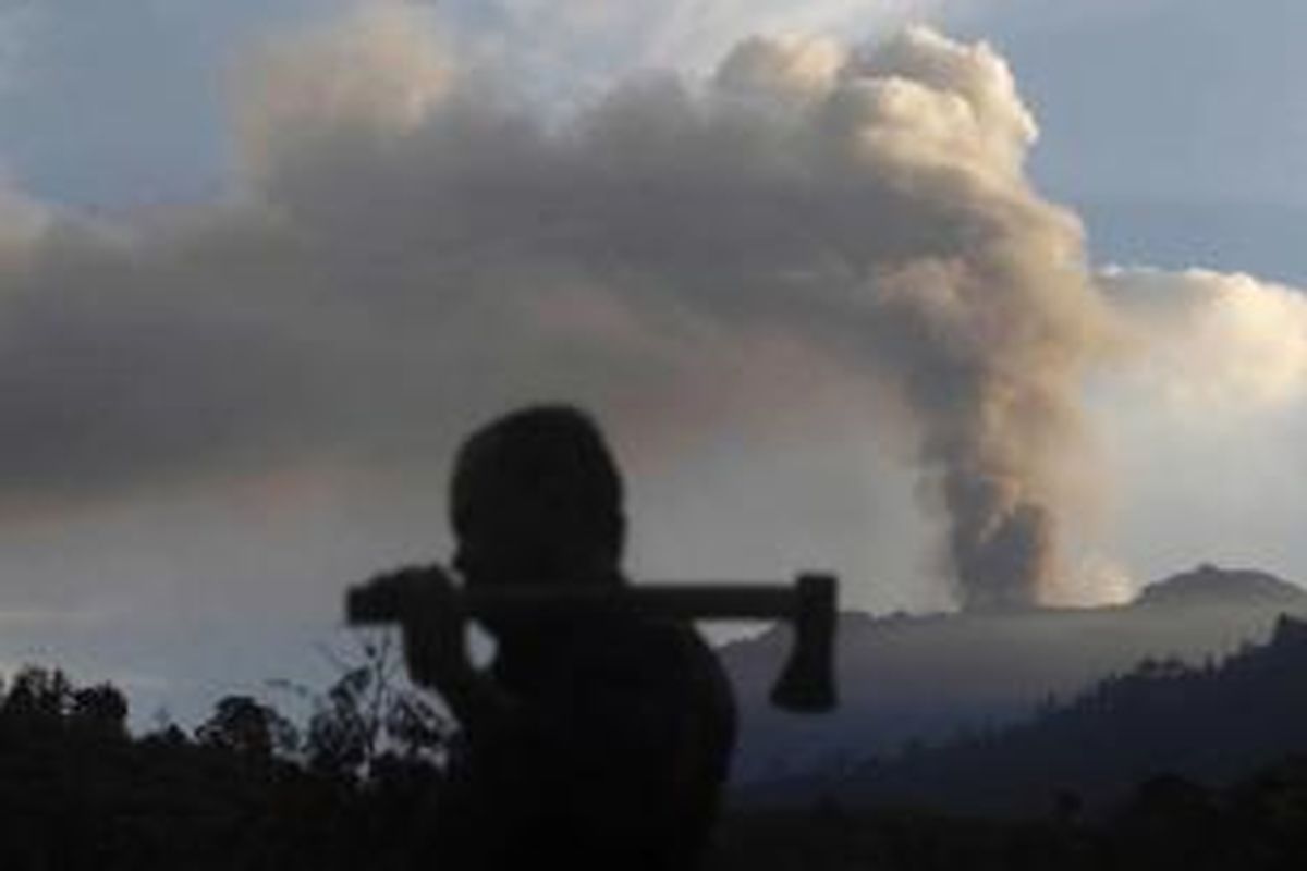 Petani melintas dengan latar belakang letusan Gunung Raung terlihat dari Melaten, Jawa Timur, 12 Juli 2015. Letusan Gunun Raung telah mengakibatkan sejumlah bandara lokal di Jawa Timur dan Bandara Ngurah Rai Bali sempat ditutup.