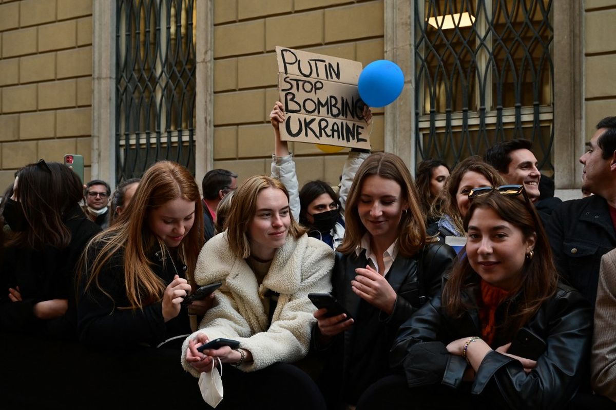 Seorang perempuan berdiri memegang spanduk bertuliskan Putin stop bombing Ukraine. Perempuan ini berdiri bersama banyak orang yang berada di depan catwalk Giorgio Armani untuk koleksi Fall/Winter 2022/2023, di hari keenam Milan Fashion Week di Milan, Italia, Minggu (27/2/2022) 