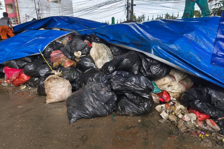 Tumpukan sampah di Kolong Flyover Ciputat ditutupi terpal untuk mengurangi dampak bau sekaligus agar tidak ada warga yang membuang sampah sembarangan di sana, Minggu (14/12/2025).