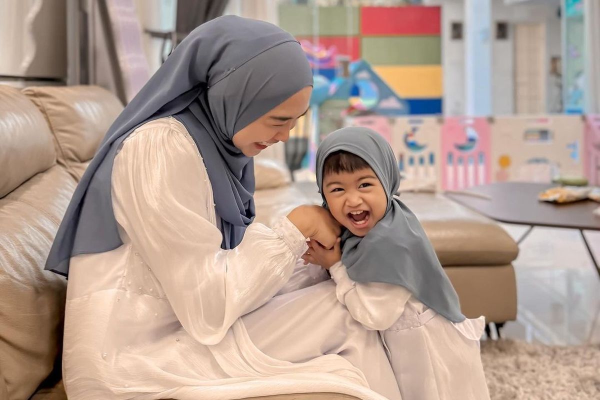 Selebgram Ria Ricis pakai baju gamis shimmer warna putih polos dipadukan dengan hijab warna biru muda. 