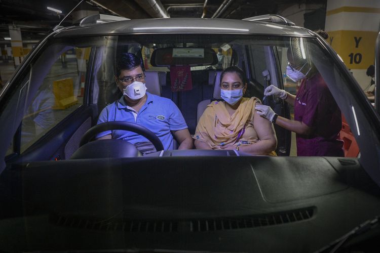 A health worker inoculates a woman sitting inside a car with the jab of Covishield vaccine against the Covid-19 coronavirus during a drive-through vaccination camp set up in the basement of a shopping mall in Vashi on September 8, 2021. (Photo by Indranil MUKHERJEE / AFP)