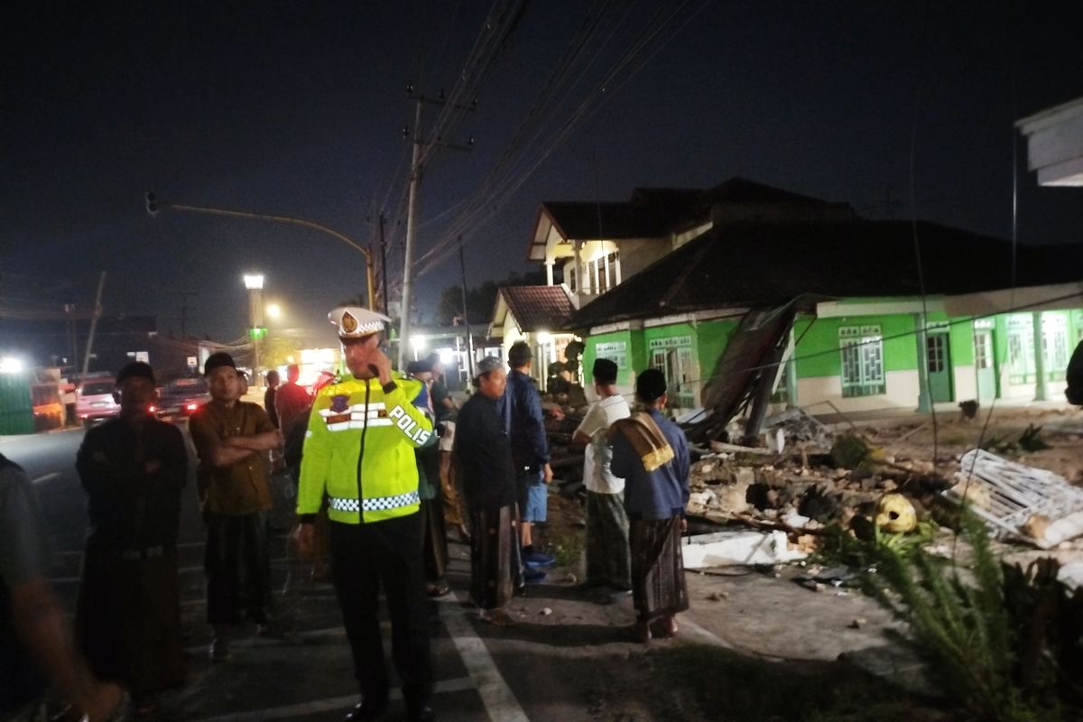Warga dan polisi berada di lokasi kecelakaan meninjau kondisi rumah warga usai ditabrak tiga kendaraan. Pagar rumah warga di Desa Burneh, Kecamatan Burneh, Bangkalan rusak, Sabtu (7/6/2025). 