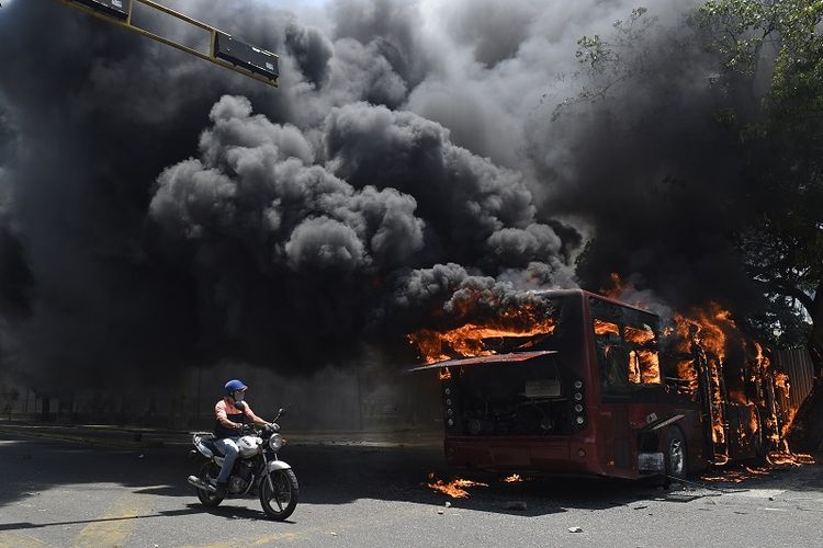 Bus pemerintah dibakar selama bentrokan dengan tentara yang setia kepada Presiden Venezuela Nicolas Maduro. Peristiwa ini terjadi di sekitar pangkalan militer La Carlota di Caracas pada Selasa (30/4/2019). (AFP/Federico Parra)