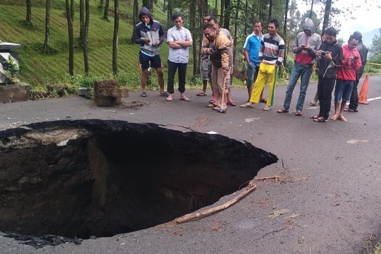 Warga melihat lubang besar akibat hujan deras semalaman yang juga membuat tebing longsor menutupi ruas jalan provinsi Brebes-Tegal, tepatnya di jalan Desa Batursari Kecamatan Sirampog, Kabupaten Brebes, Jawa Tengah, Sabtu (13/2/2021). 