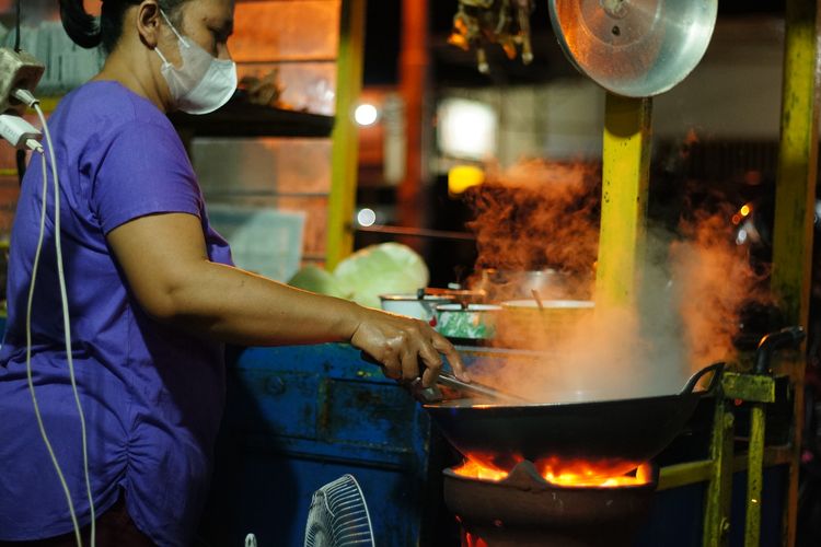 Ilustrasi pemiliki warung Bakmi Jawa Pak Geno sekarang, sedang memasak bakmi jawa. 