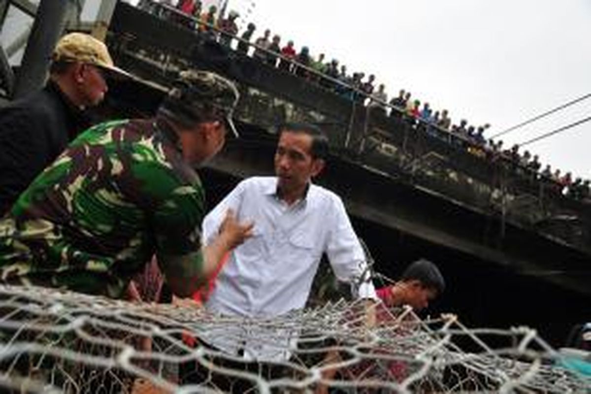 Gubernur DKI Jakarta Joko Widodo berbincang dengan anggota TNI AD saat meninjau kembali tanggul Kanal Banjir Barat di Jalan Latuharhary, Manteng, Jakarta Pusat, Jumat (18/1/2013). Tanggul itu jebol sehingga air kanal tumpah ruah ke Jalan Teluk Betung dan Tosari sehingga mengalir ke Jalan Thamrin dan Jalan Sudirman. Selain itu, perjalanan kereta api tidak beroperasi karena rel kereta api arah ke Stasiun Tanah Abang dan Manggarai terendam.