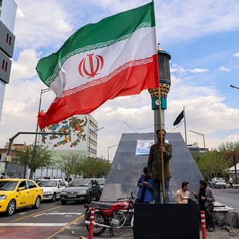 Seorang pria berdiri membawa bendera Iran di persimpangan Valiasr Square di Teheran, Senin (6/4/2026). Amerika Serikat dan Iran pada Rabu (8/4/2026) mengumumkan gencatan senjata selama dua minggu. Respons Negara-negara soal Gencatan Senjata Iran-AS: Sambut Positif dan Desak Perdamaian Abadi