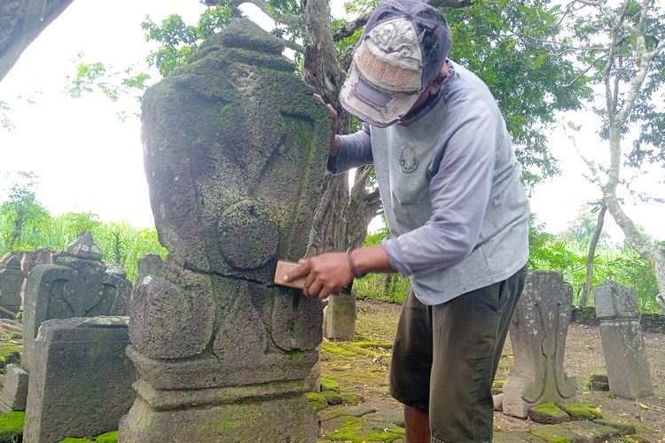 Juru Pelihara Situs Nduro, Sugeng (47), saat membersihkan lumut yang menempel di nisan pada kompleks pemakaman kuno Dusun Nanggungan, Desa Watudandang, Kecamatan Prambon, Kabupaten Nganjuk, Jawa Timur, Rabu (13/3/2024)