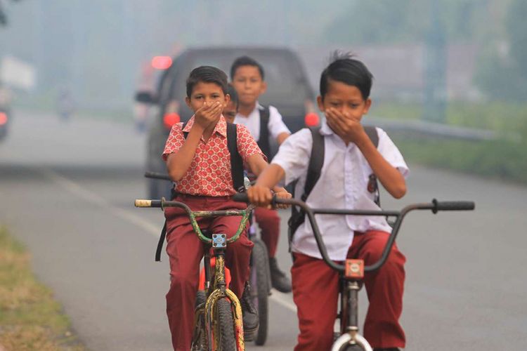 Sejumlah siswa naik sepeda sambil menutup hidung akibat kabut asap di Desa Suak Raya, Kecamatan Johan Pahlawan, Aceh Barat, Aceh, Rabu (30/1/2019). Kebakaran lahan gambut yang terjadi di kabupaten setempat menyebabkan jalan lintas diselimuti kabut asap dengan jarak pandang 30 - 70 meter.