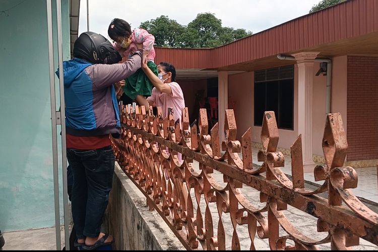 Jenny dan Patar Tampubolon terpaksa menyeberangkan anaknya melewati besi dinding pagar karena akses jalan ke rumahnya di Kecamatan Medan Denai ditutup tetangganya 