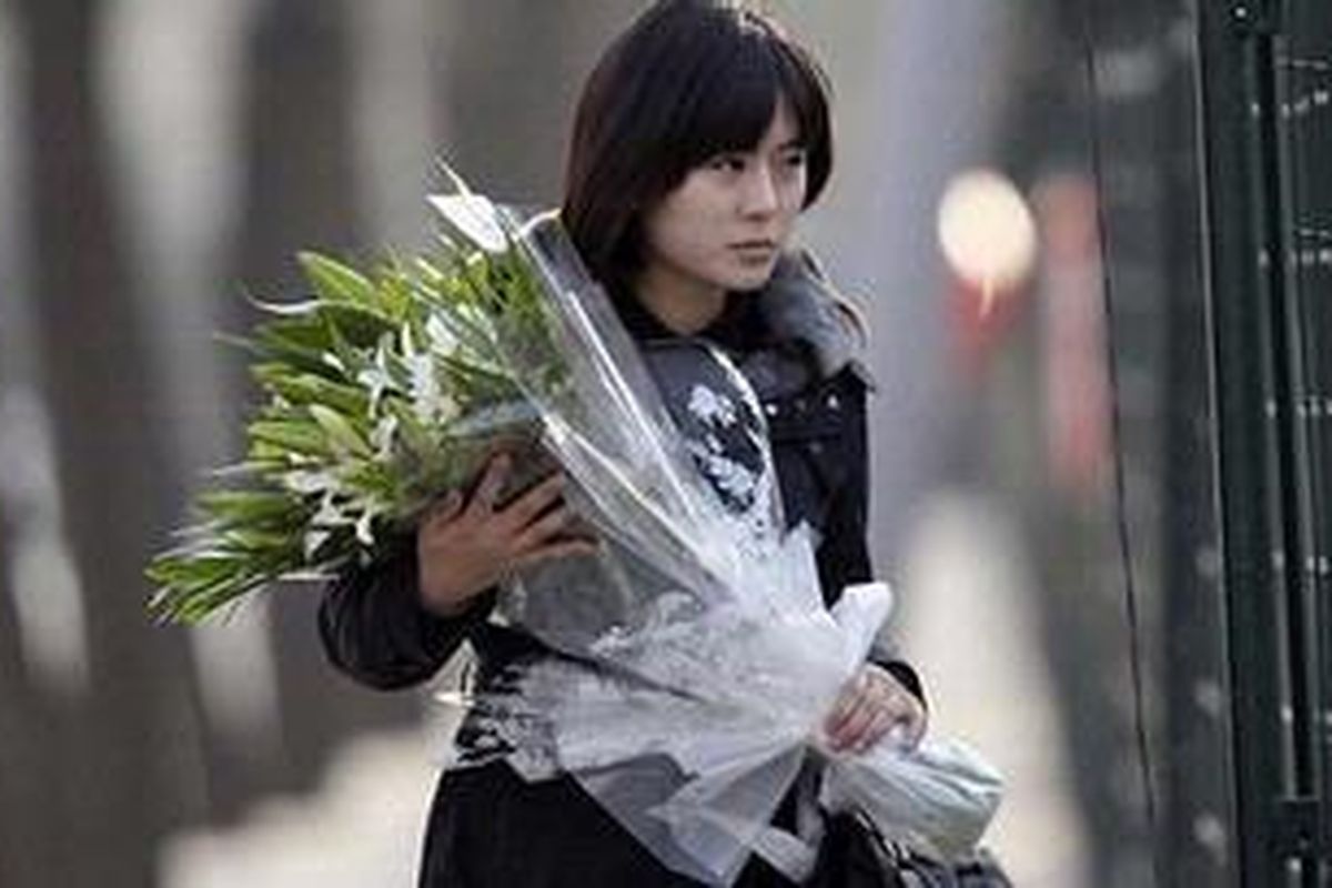 Seorang warga Korea Utara membawa bunga tanda duka cita atas kematian pemimpin Korea Utara, Kim Jong-il, saat melewati pagar kedutaan besar Korea Utara di Beijing, China, Senin (19/12/2011).