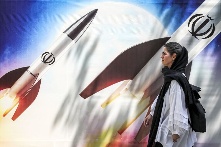 Seorang wanita berjalan melewati spanduk yang menggambarkan peluncuran rudal berlambang Republik Iran di pusat Kota Teheran, Senin (15/4/2024). Iran meluncurkan ratusan drone ke wilayah Israel, Minggu (14/4/2024), sebagai balasan Israel yang menghancurkan kedutaan besar Iran di Damaskus pada 1 April 2024. 