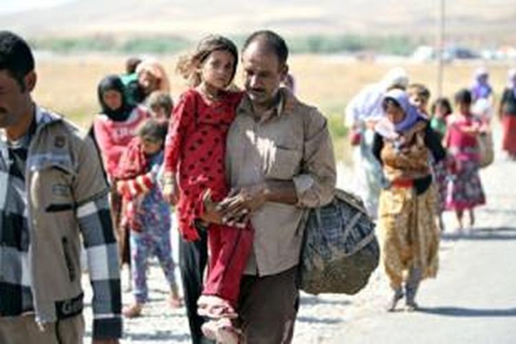 Seorang pengungsi Yazidi Irak mengendong putrinya saat melintasi perbatasan Suriah, Senin (11/8/2014). Sekitar 20.000 warga minoritas Yazidi masih terjebak di Gunung Sinjar. 