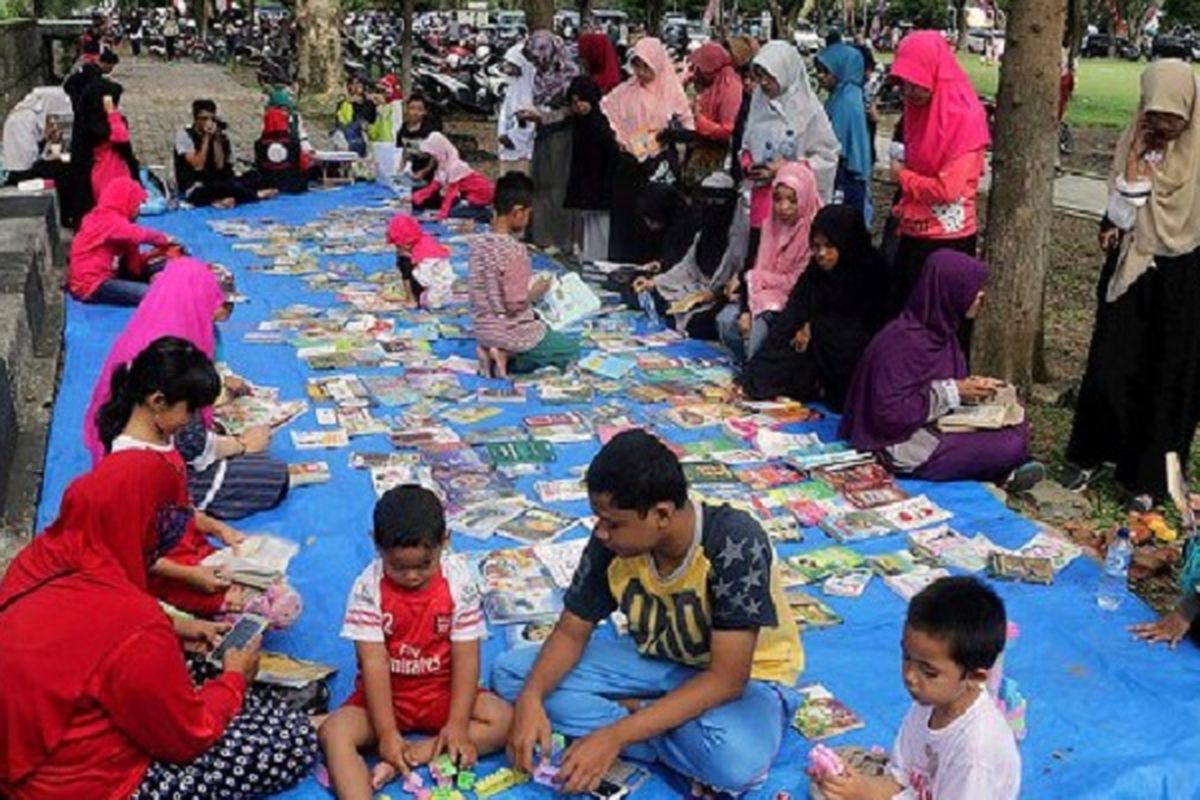 Warga membaca buku di arena pustaka di lapangan terbuka Blang Padang, Banda Aceh, Aceh, Minggu (5/3). Komunitas Rumah Baca Aneuk Nanggroe membuka pustaka di ruang publik setiap hari Minggu untuk mendekatkan buku dengan warga sehingga menumbuhkan minat baca. 