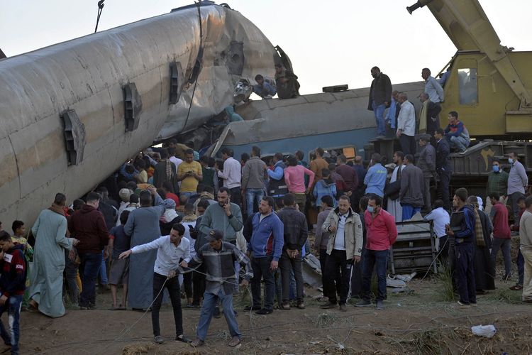 Warga berkerumun mengelilingi puing-puing kecelakaan kereta api Mesir yang melibatkan dua KA di distrik Tahta, provinsi Sohag, sekitar 460 km selatan Kairo, pada Jumat (26/3/2021). Total 20 orang tewas dan 199 luka-luka dalam insiden ini.