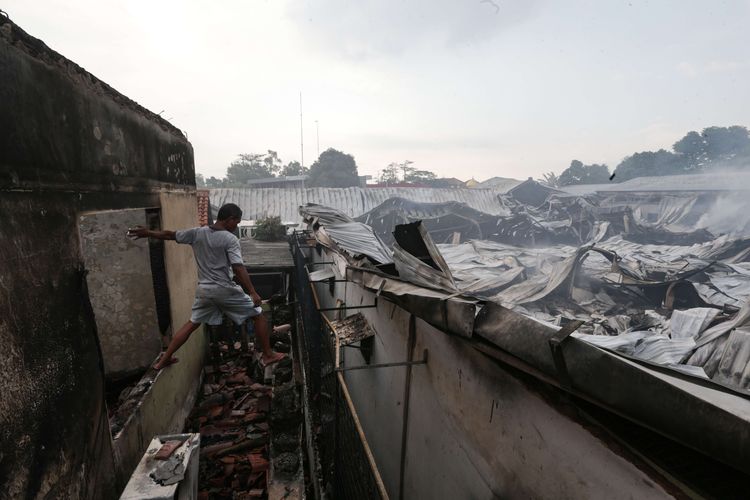 Warga melihat rumahnya yang ikut terbakar saat peristiwa  kebakaran melanda gudang JNE Express di Jalan Pekapuran, Cimanggis, Depok, Senin (12/9/2022). Kebakaran dilaporkan terjadi sekitar pukul 04.51 WIB, api berhasil dipadamkan sekitar pukul 08.57 WIB.