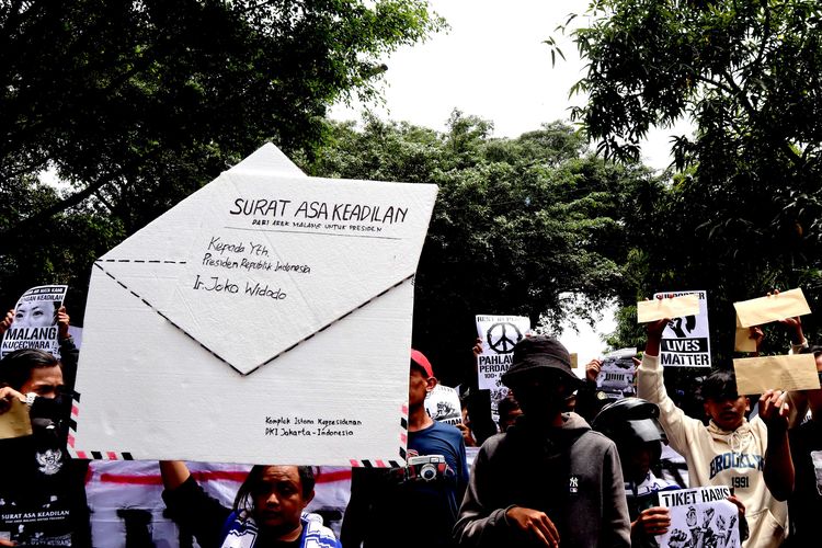 Seorang suporter Arema FC, membentangkan miniatur amplop saat menggelar aksi kirim Surat dari Aremania untuk Presiden Jokowi Menuntut Usut Tuntas Tragedi Kanjuruhan di Kantor Pos Kota Malang, Kamis (17/11/2022) siang.
