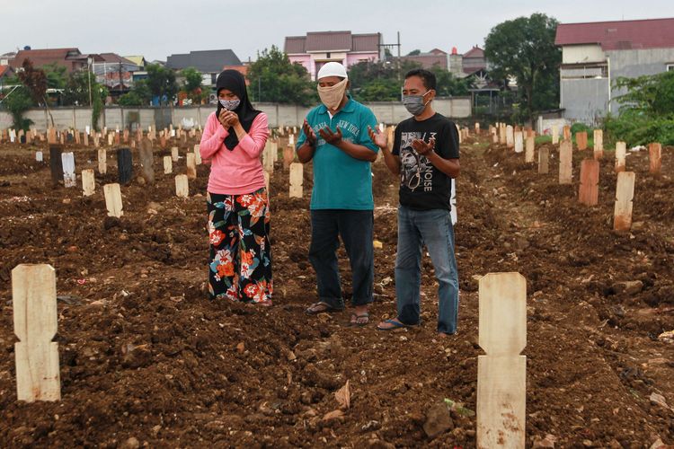 Three people pray before the grave of a loved one who was killed by Covid-19