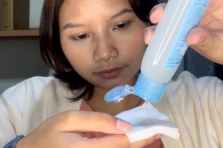 Model sedang menuangkan micellar water pada kapas.