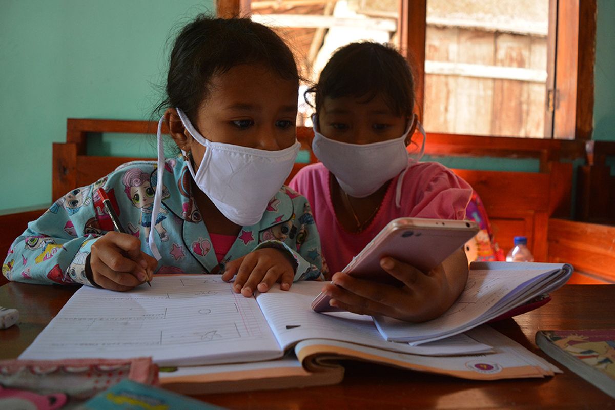 Dua siswa SDN Marmoyo, mengerjakan tugas dengan berkelompok menggunakan gawai secara bergantian di rumah warga Desa Marmoyo, Kecamatan Kabuh, Kabupaten Jombang, Jawa Timur, Rabu (22/7/2020). Banyaknya siswa yang tidak punya gawai dan akses jaringan internet menjadi kendala utama pelaksanaan pembelajaran jarak jauh bagi pelajar yang tinggal serta sekolah di daerah pelosok Kabupaten Jombang, sehingga mereka harus mengerjakan tugas secara berkelompok dan menumpang di rumah warga yang bisa mengakses jaringan internet.