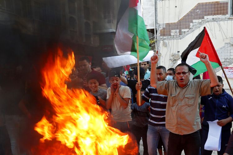 Para pengunjuk rasa mengibarkan bendera Palestina sambil meneriakkan slogan-slogan anti-Israel sambil membakar representasi buatan tangan dari bendera Israel selama protes terhadap pawai oleh ultranasionalis Yahudi melalui Yerusalem timur, di sepanjang jalan-jalan Kota Gaza, Selasa, 15 Juni 2021.
