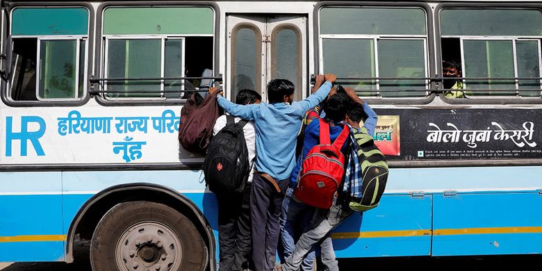 Para pekerja migran bergantungan ke sebuah pintu bus yang bergerak saat mereka kembali ke desa mereka, saat diberlakukan lockdown nasional selama 21 hari untuk membatasi penyebaran penyakit virus corona (COVID-19) di Ghaziabad, pinggiran kota New Delhi, India, Minggu (29/3/2020).