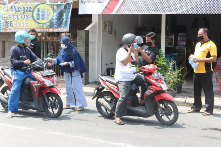 Aipda Purnomo dan keluarga saat membagikan masker secara gratis kepada warga yang kebetulan melintas di sekitar pertigaan lampu merah Kecamatan Deket, Lamongan.