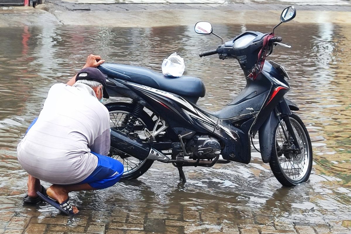 Meji (70), tampak mencuci sepeda motornya di genangan banjir, Jalan Raya Duta Pelni, Jumat (1/12/2023) siang.