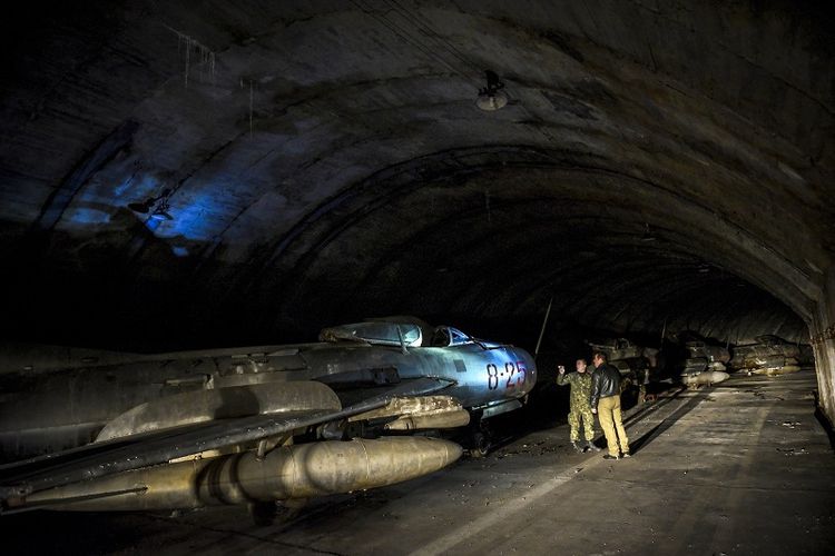 Personel militer Albania berdiri di dekat sebuah jet tempur MIG-19 yang disimpan di terowongan utama pangkalan udara Gjader di dekat kota Lezhe.