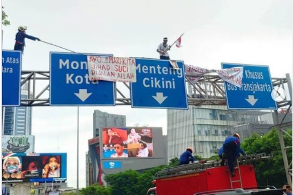 Seorang pria memanjat rambu lalu lintas di Jalan Sudirman, Jakarta Pusat, Senin (2/11/2020). Dia tampak membentangkan spanduk di papan rambu tersebut.