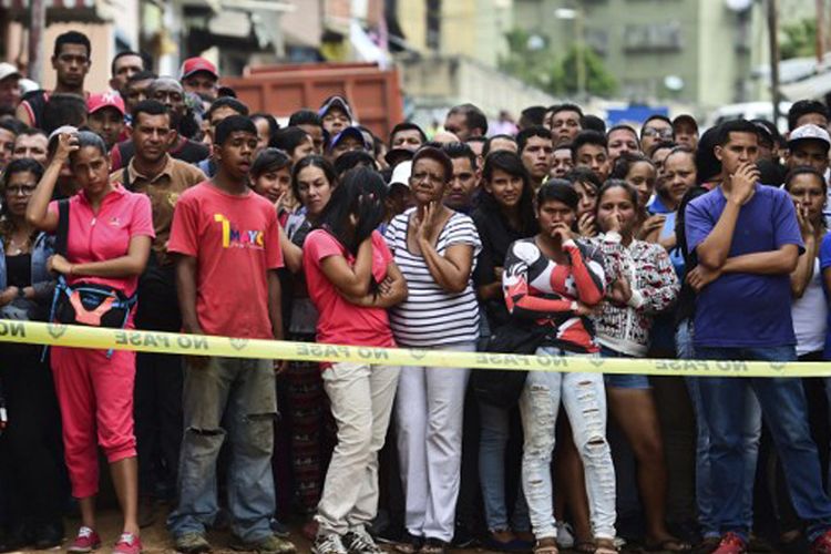 Warga menyaksikan para polisi yang bekerja membereskan sebuah toko roti yang hancur akibat kerusuhan di perkampungan El Valle, di Caracas, Jumat (21/4/2017).  