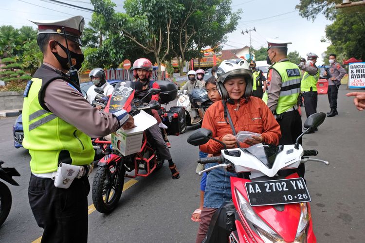 Polisi membagikan masker kepada pengendara sepeda motor saat mengatur arus lalu lintas di jalur mudik di jalan utama kota Temanggung, Jawa Tengah Sabtu  (30/4/2022). Personel polisi yang bertugas di pos pengamanan Lebaran 2022 selain mengatur lalu lintas dan menjaga keamanan jalur mudik juga mengkampanyekan penerapan protokol kesehatan dengan membagikan masker.