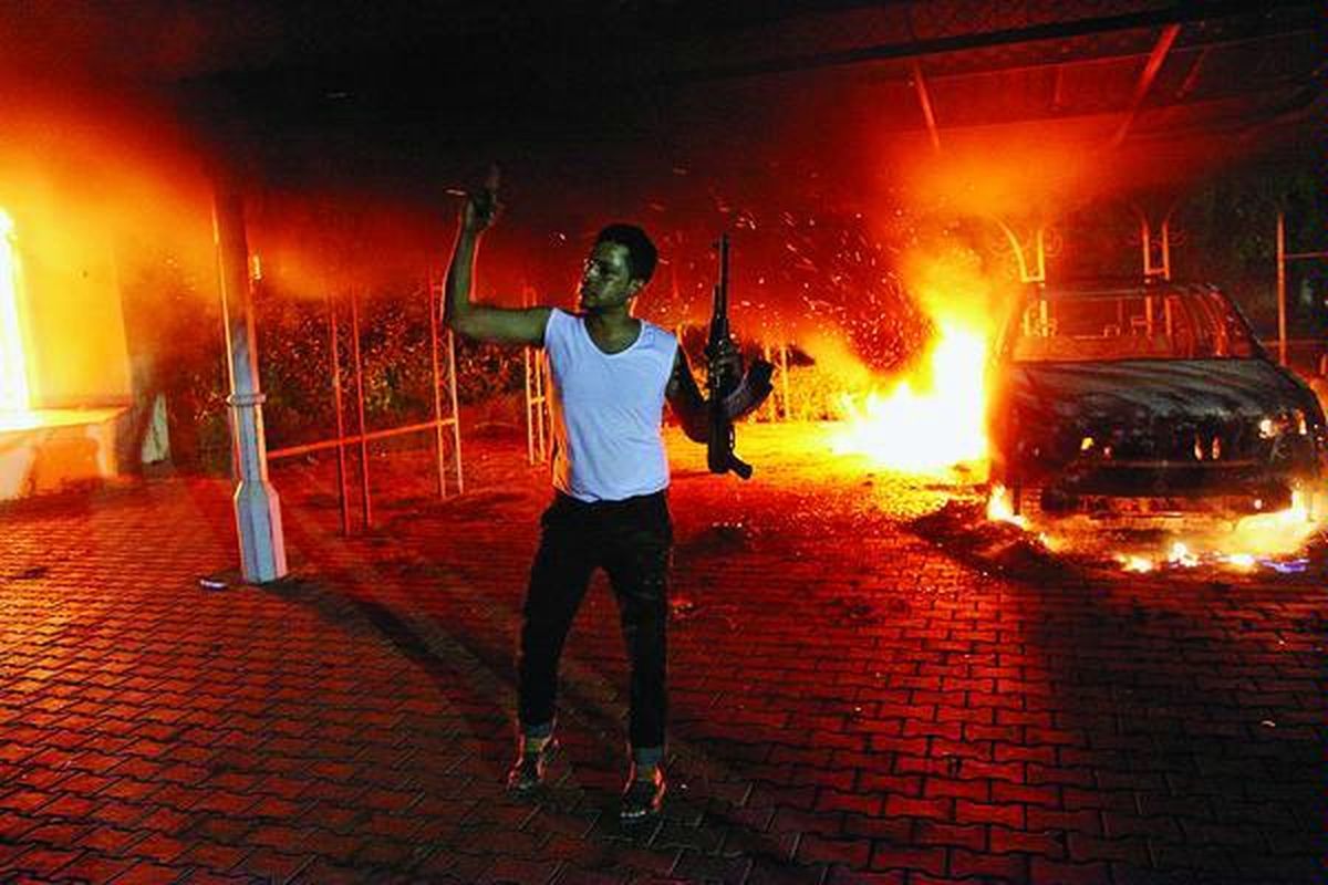 Seorang lelaki dengan senapan laras panjang di depan mobil-mobil yang dibakar di halaman dalam kantor Konsulat Amerika Serikat  di Benghazi, Libya, Selasa (11/9) larut malam. Akibat serbuan massa tersebut, Duta Besar AS untuk Libya Christopher  Stevens dan tiga anggota staf Konsulat AS tewas.