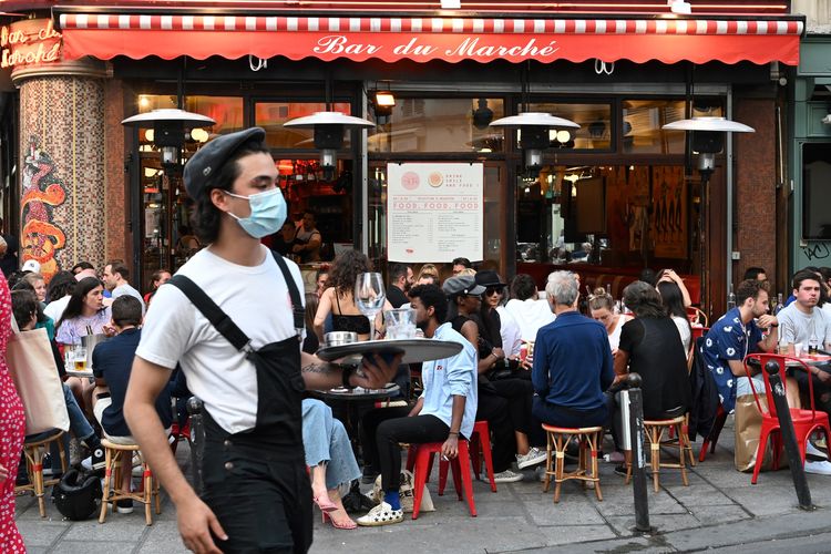 Seorang pelayan mengenakan masket wajah saat melayani pelanggan yang makan dan minum di teras cafe restoran Le Bar du Marche, di Paris, Perancis, 2 Juni 2020. Restoran dan cafe mulai buka setelah Perancis melonggarkan kebijakan lockdown di negaranya.