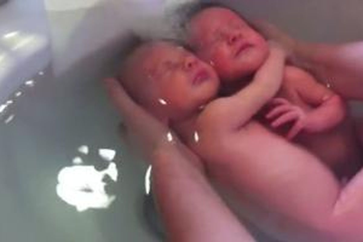 Dua bayi kembar menikmati waktu mandi sembari berpelukkan.