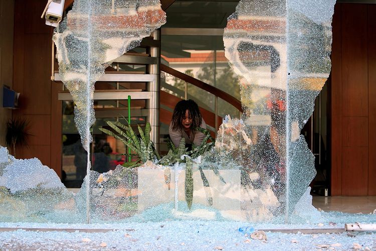 Seorang pekerja membersihkan kaca pecah di depan sebuah bank setelah aksi protes malam sebelumnya atas kesulitan ekonomi di Sidon, Lebanon, Rabu (29/4/2020). Wabah Covid-19 yang masih menghantui dunia dan berimbas pada banyak sektor kehidupan, memunculkan aksi unjuk rasa di sejumlah negara.