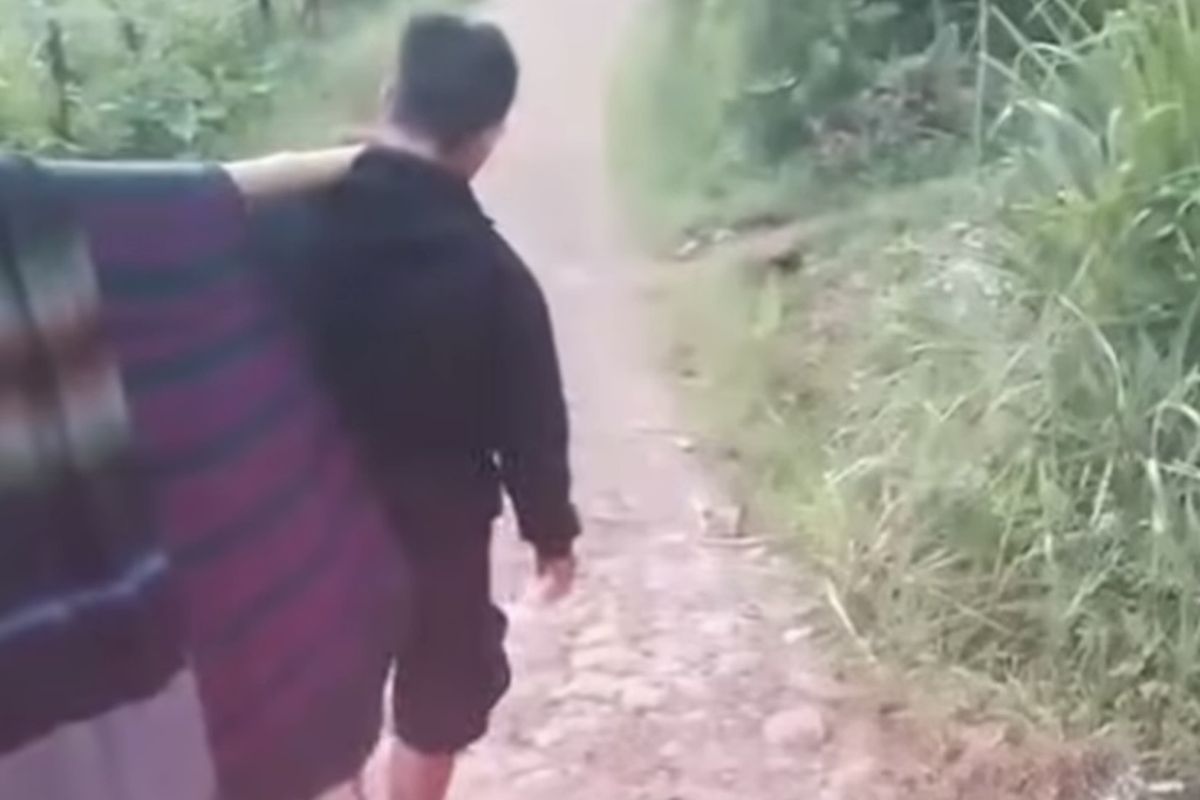 Tangkapan layar video viral Seorang warga sakit di Kampung Buah Batu, Desa Sukasari, Kecamatan Gununghalu, Kabupaten Bandung Barat (KBB), Jawa Barar terpaksa ditandu dengan sarung dan bambu sejauh lebih dari satu kilometer karena ambulans tidak mampu mencapai rumahnya, Selasa (2/12/2025).