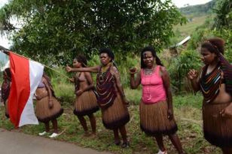 Perempuan Papua mengenakan busana tradisional dan mengibarkan Bendera Merah Putih saat menyambut kedatangan Presiden Joko Widodo dan rombongan di Jayapura, Papua, 9 Mei 2015.