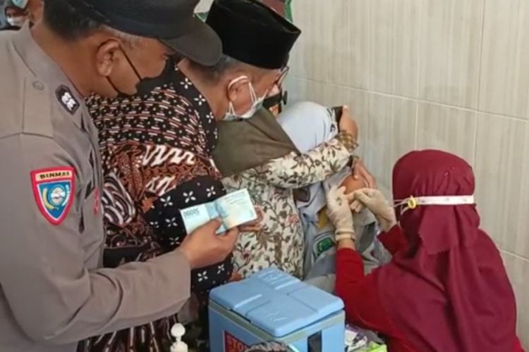 Kanit Binmas Polsek Manyar Aiptu Rozi (kiri), menyiapkan uang tunai Rp50 ribu bagi Tri Luwes Prasetya yang phobia jarum suntik sebagai hadiah saat menjalani vaksinasi, Jumat (24/9/2021).