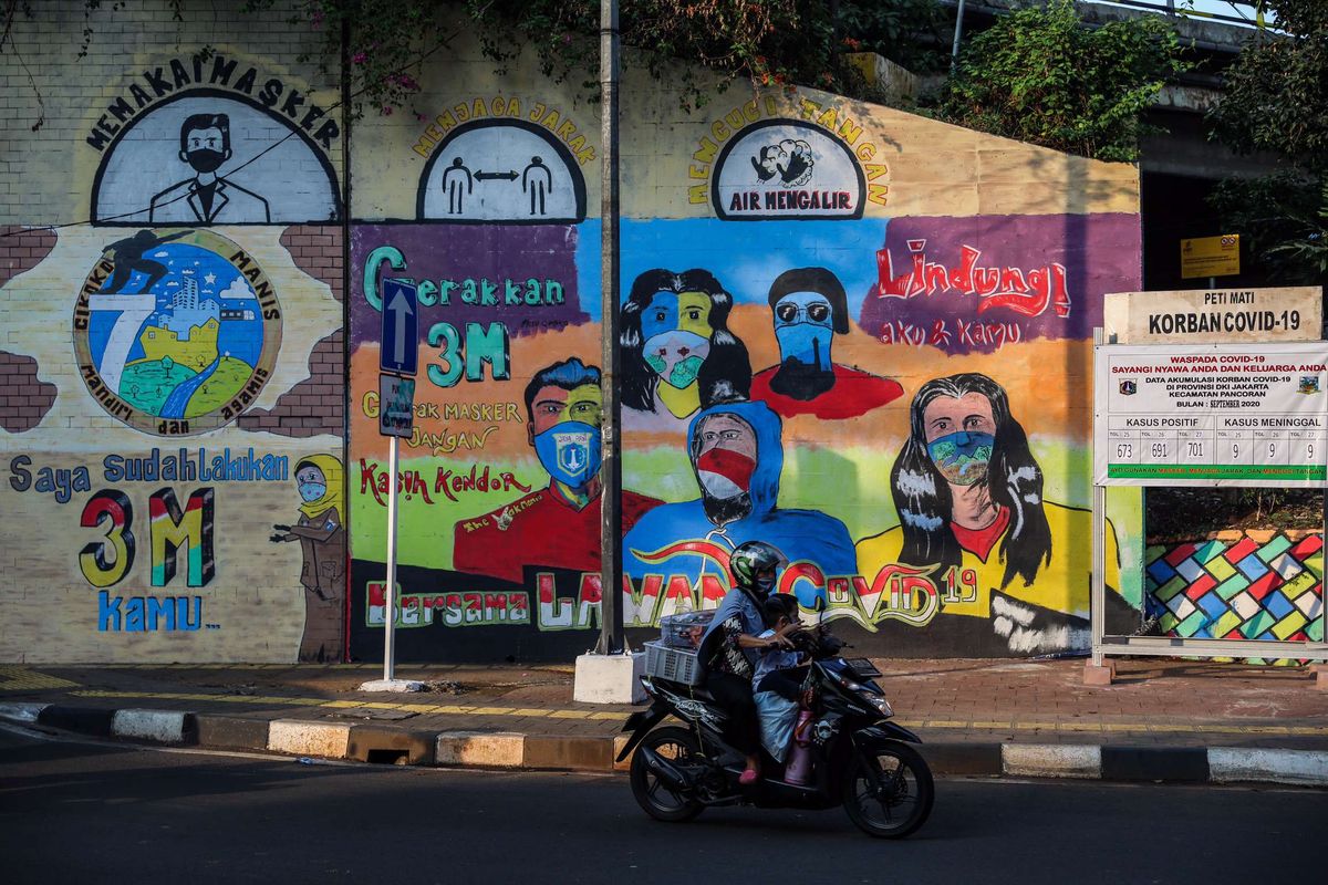 Warga menggunakan sepeda motor saat melintasi mural berisi pesan ajakan menggunakan masker di Cikoko, Pancoran, Jakarta Selatan, Sabtu (3/10/2020). Pembatasan sosial berskala besar (PSBB) di Jakarta untuk mengendalikan penularan Covid-19 telah memasuki pekan ketiga.
