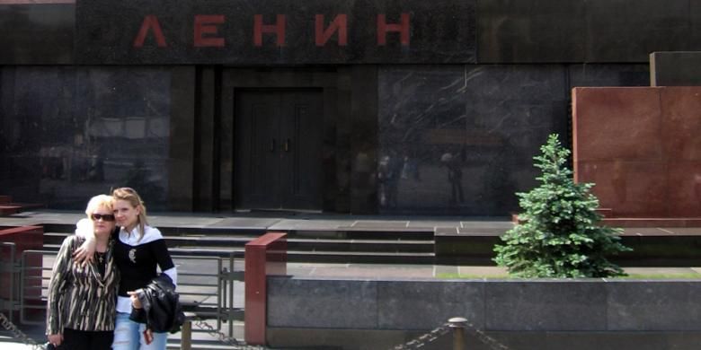Dua wisatawan sedang berpose di depan pintu masuk mausoleum tempat jasad Tokoh Komunis Rusia Vladimir Lenin disemayamkan. Pada hari-hari tertentu, tempat ini dibuka untuk umum, dan pengunjung dapat melihat jenazah Lenin yang diletakkan dalam peti kaca.