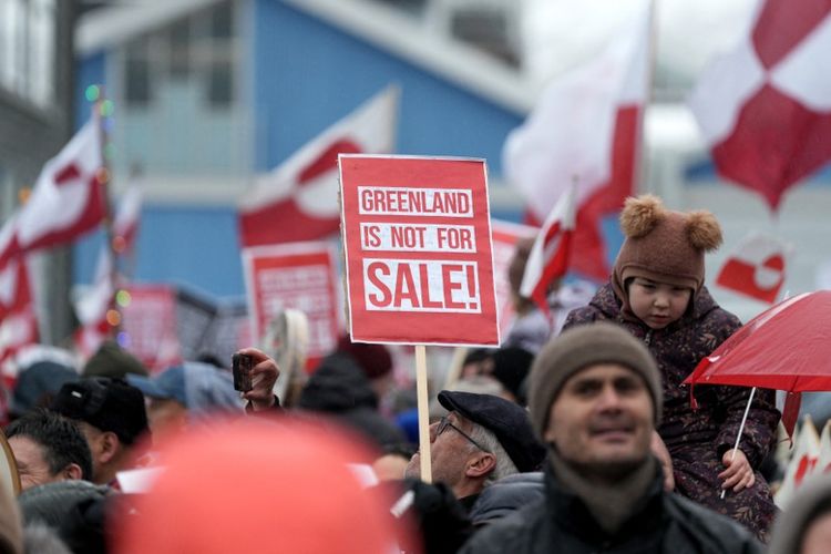 Orang-orang mengibarkan bendera Greenland saat mereka berpartisipasi dalam demonstrasi yang mengumpulkan hampir sepertiga penduduk kota untuk memprotes rencana Presiden AS untuk mengambil alih Greenland, pada 17 Januari 2026 di Nuuk, Greenland. Presiden AS Donald Trump meningkatkan upayanya untuk mengakuisisi Greenland, mengancam beberapa negara Eropa dengan tarif hingga 25 persen sampai pembelian wilayah Denmark tersebut tercapai. 