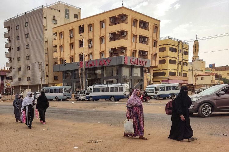 Para wanita berjalan di sepanjang jalan di selatan Khartoum pada 24 April 2023, saat pertempuan antara pasukan dua jenderal sedang berlangsung.