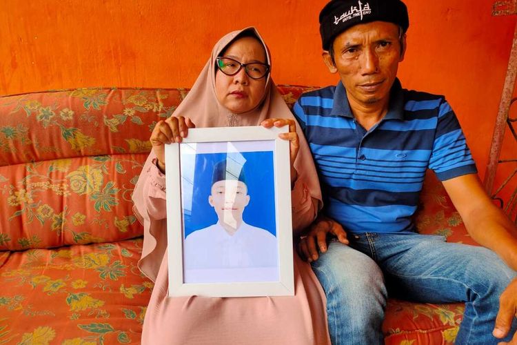 Soimah bersama suaminya Rusdi memegang foto anak mereka AM semasa hidup sebelum akhirnya tewas lantaran diduga dianiaya.