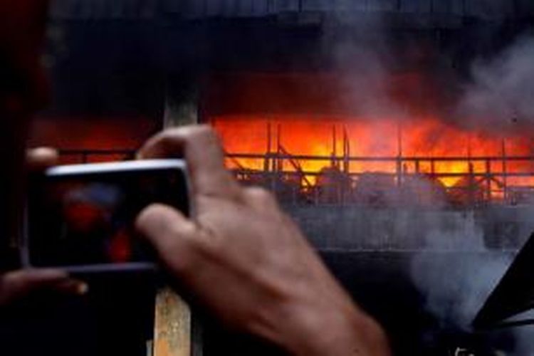 Pemilik kios mengabadikan api yang melalap Pasar Senen, Jakarta Pusat, Jumat (25/4/2014). Sebanyak 43 unit pemadam kebakaran dikerahkan untuk memadamkan api yang mulai berkobar sekitar pukul 04.00 WIB. Tidak ada korban dalam peristiwa tersebut namun penyebab kebakaran belum diketahui pasti.